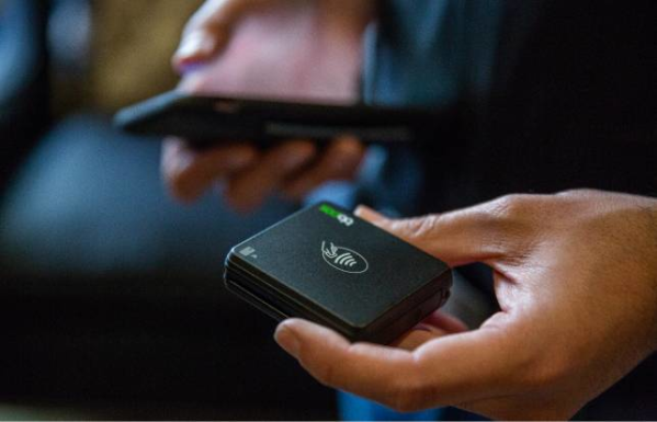 - Housecall Pro Person holding black card reader in left hand and mobile phone in right