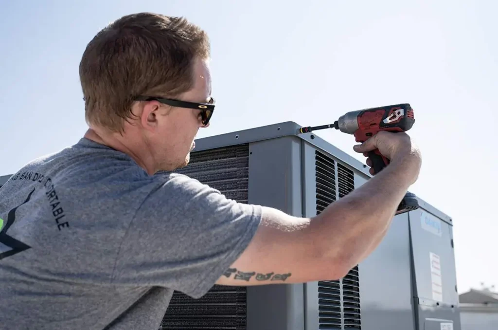 - Housecall Pro Service technician using power tool drill to unscrew HVAC unit
