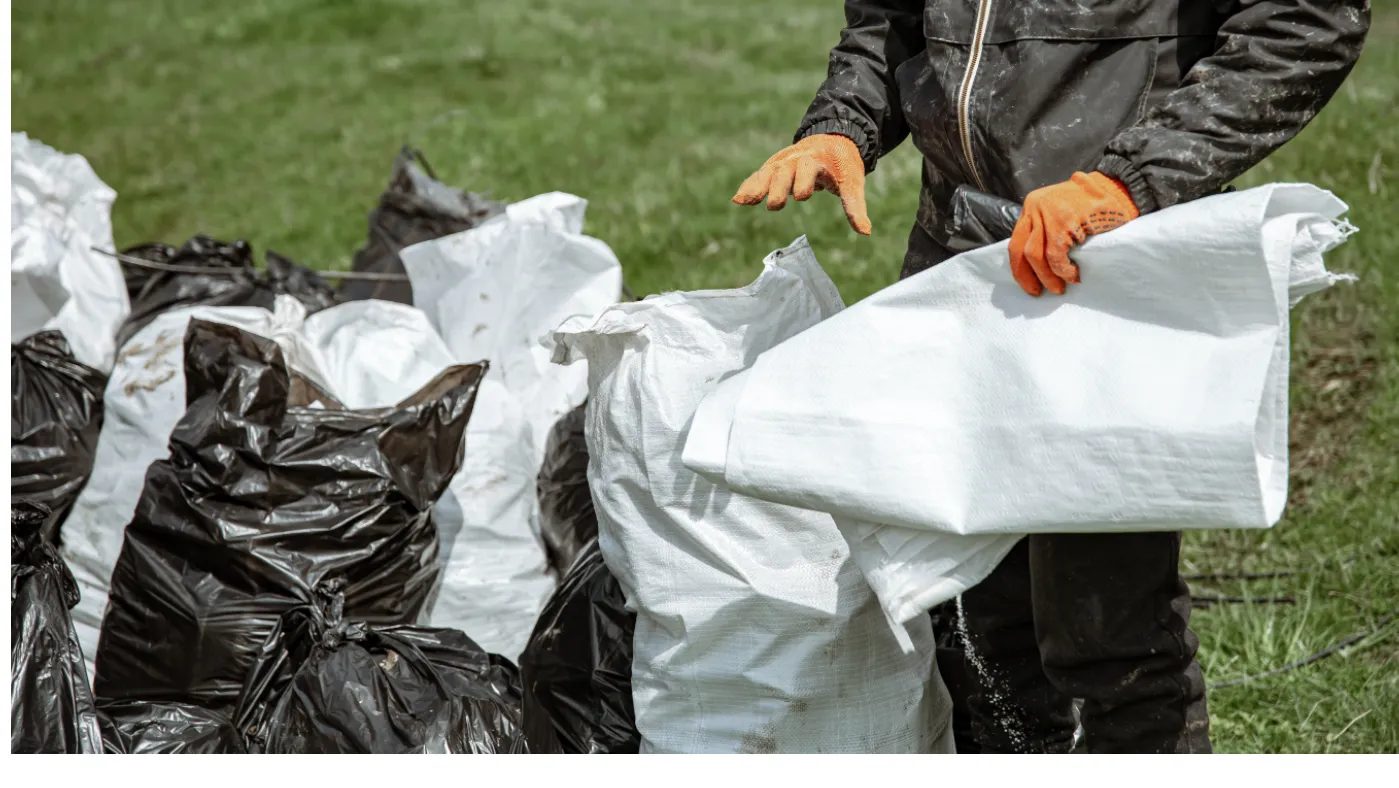 Worker wearing gloves handling white and black garbage bags for junk removal company name inspiration.