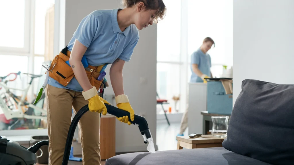 - Housecall Pro cleaning service workers working in apartment in team, they vacuuming furniture and cleaning the room