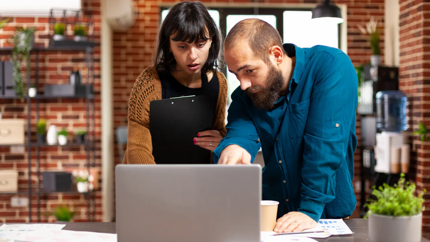 Two marketing professionals reviewing website performance and technical SEO issues on a laptop.