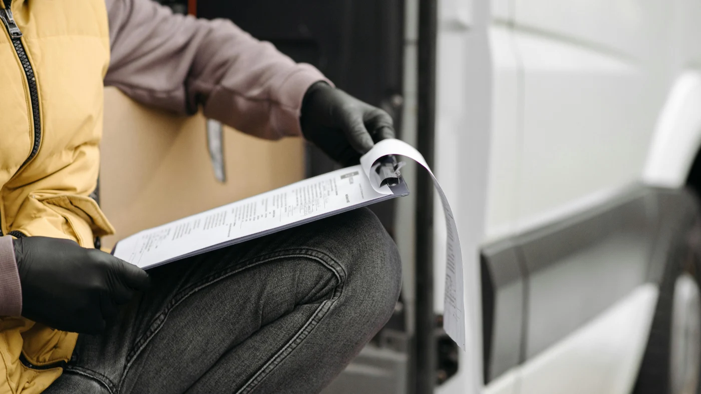 Worker reviewing a clipboard document while sitting by a vehicle.