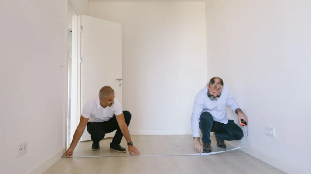Flooring contractors measuring a room to calculate square footage, material requirements, and installation costs.