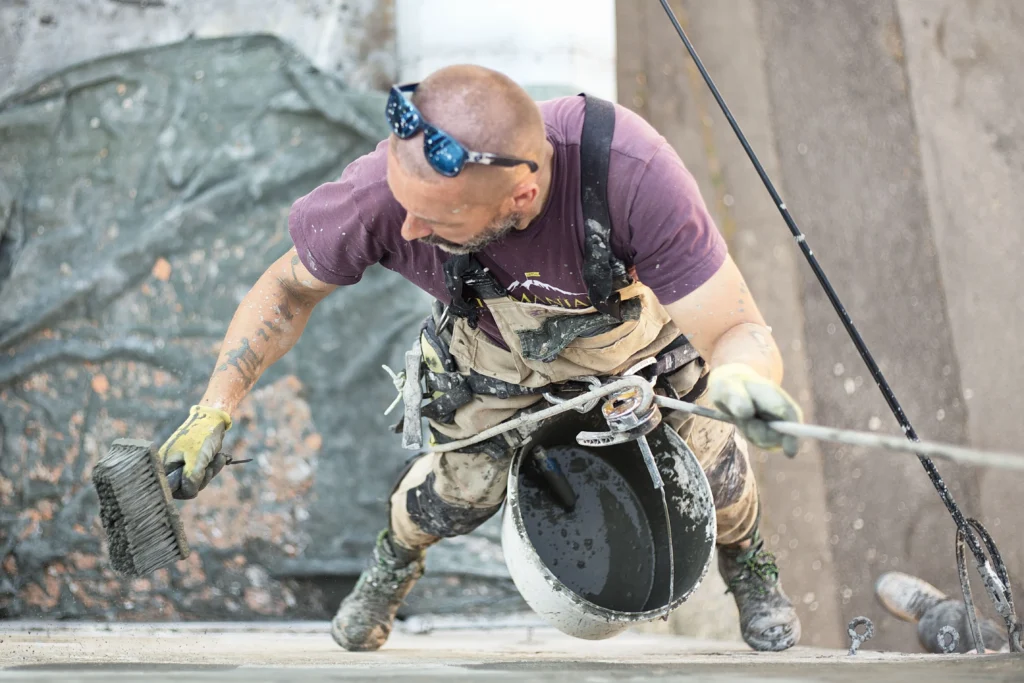 Contractor applying concrete waterproofing and protective coatings on a building exterior as part of a commercial concrete project.
