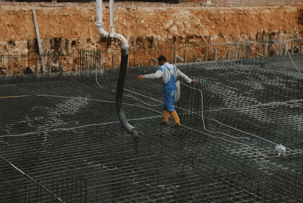 Worker walking across a reinforced steel rebar grid used to calculate concrete volume, material costs, and foundation construction pricing.