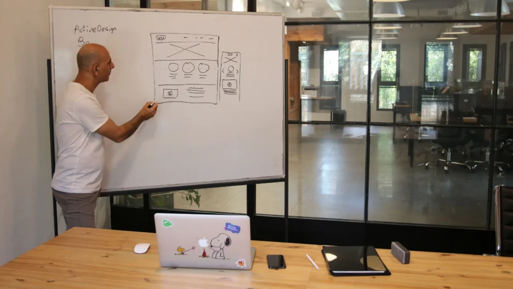 Professional designer in an office sketching a website layout on a whiteboard while explaining where to mention Klarna on a website