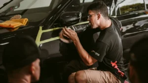 Auto detailer using a polisher on the taped-off fender of a black car during a paint correction job.