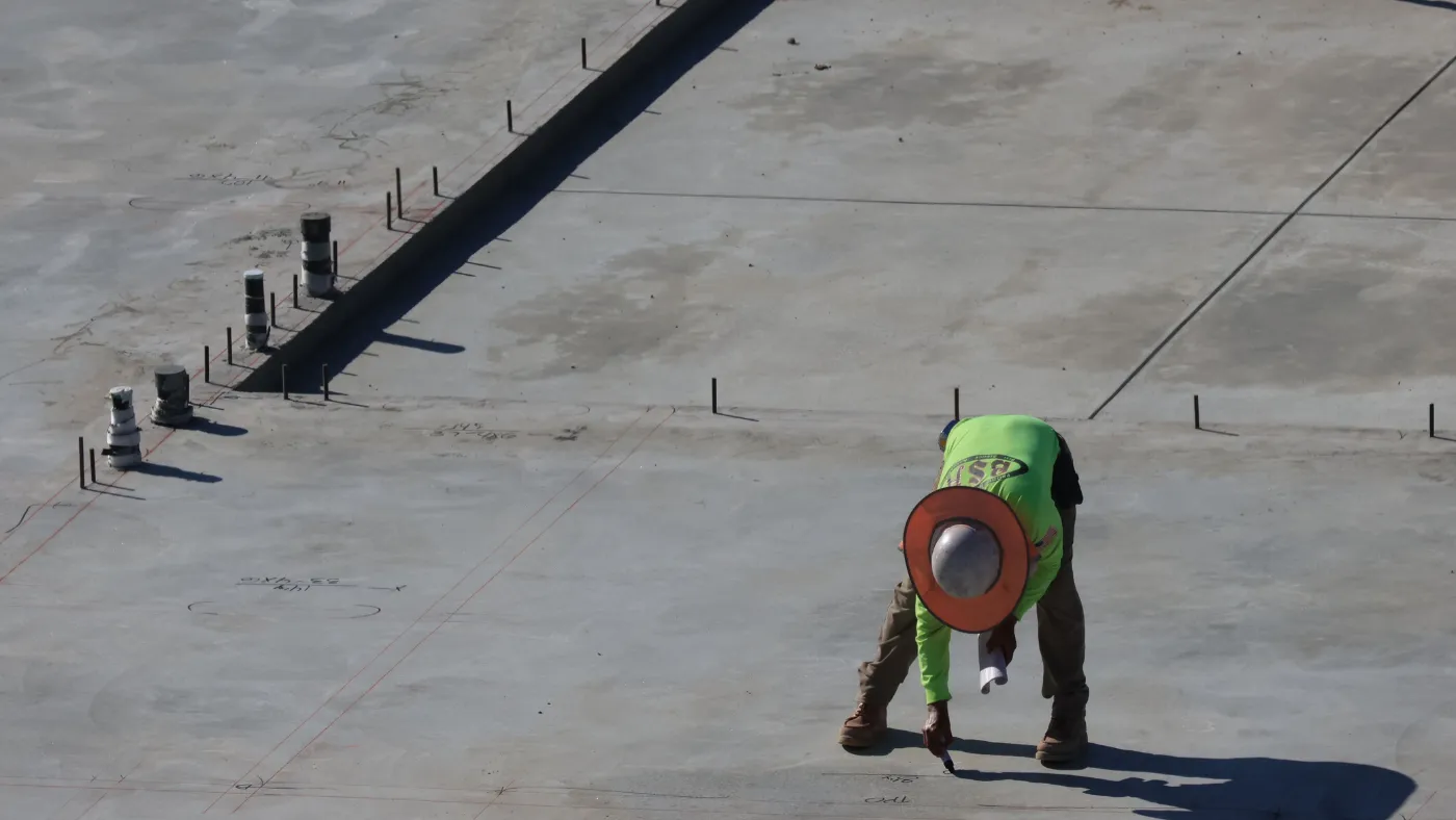 Concrete worker in a hi-vis shirt and hard hat finishing a freshly poured commercial slab on a jobsite.